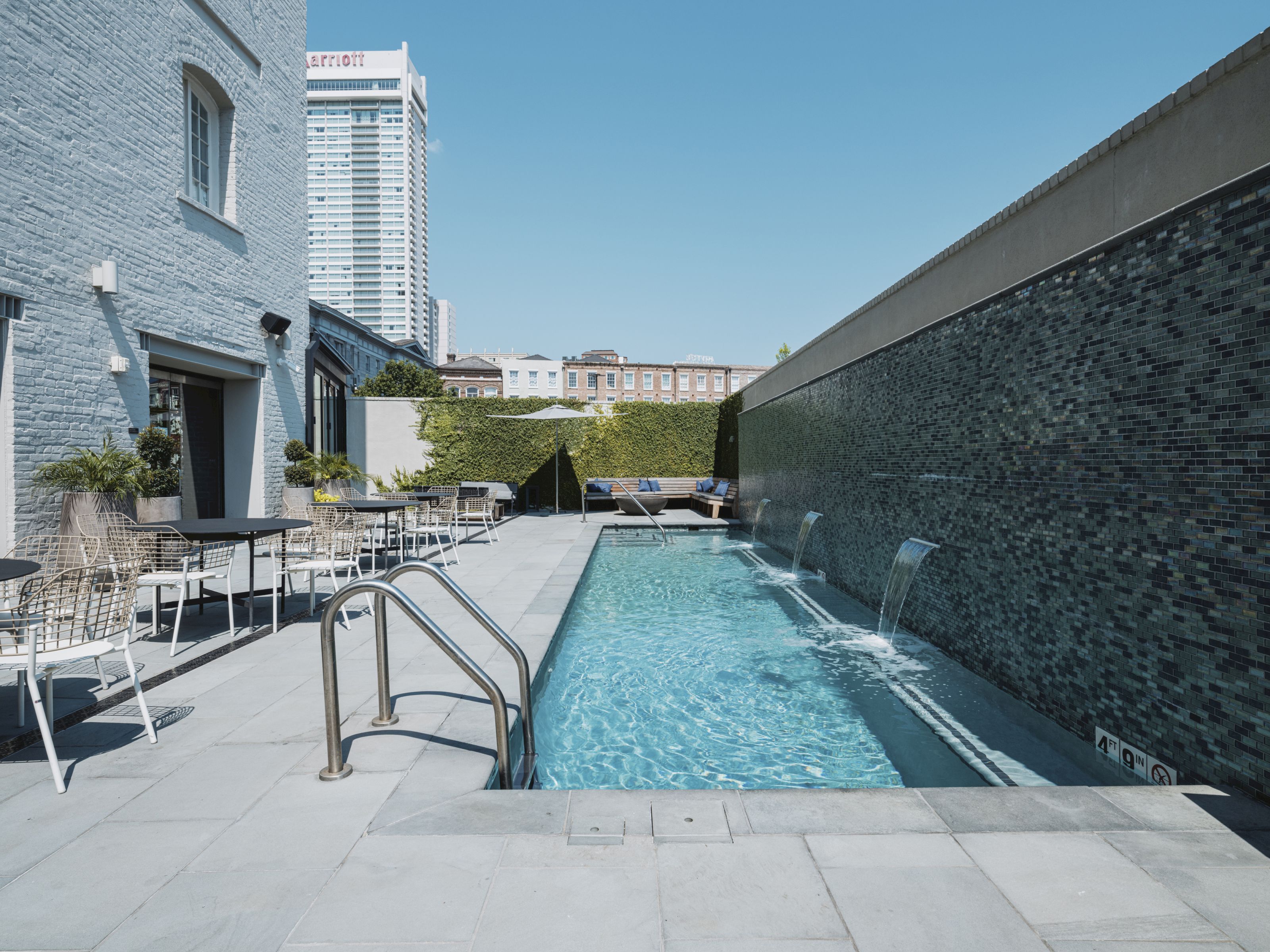 A narrow rectangular pool with water features and a seating area in an urban setting.